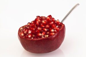 Melograno tagliato a metà con un cucchiaio pronto per essere battuto per sgranarne i semi.