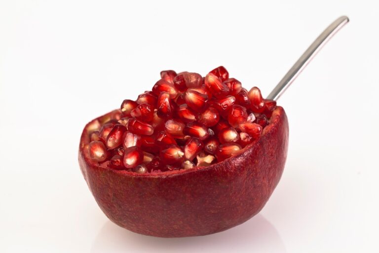 Melograno tagliato a metà con un cucchiaio pronto per essere battuto per sgranarne i semi.